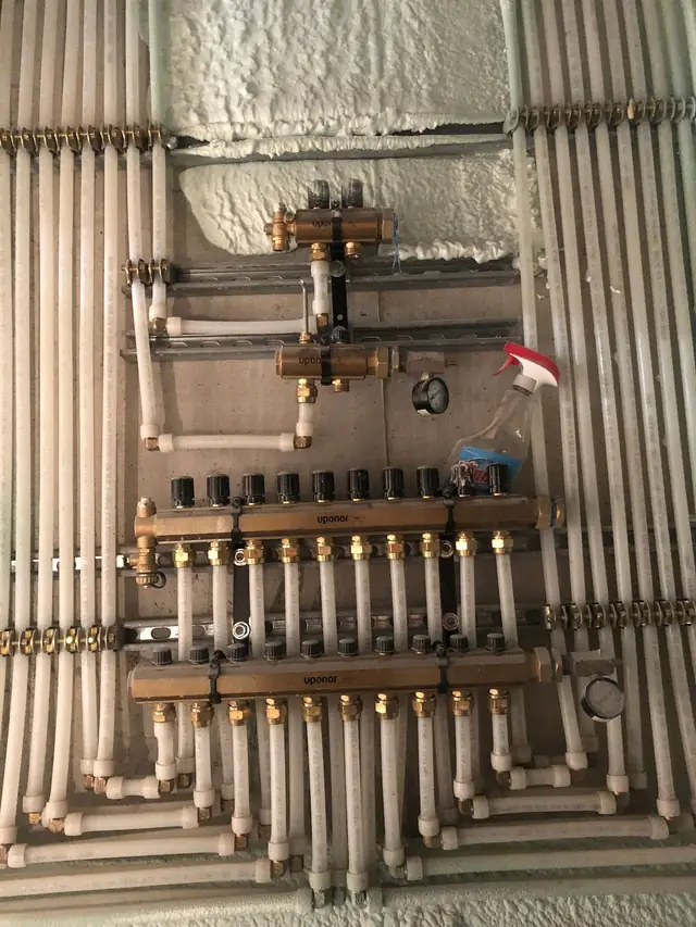 A hydronic heating manifold on a basement wall, brass valves feeding rows of insulated PEX runs