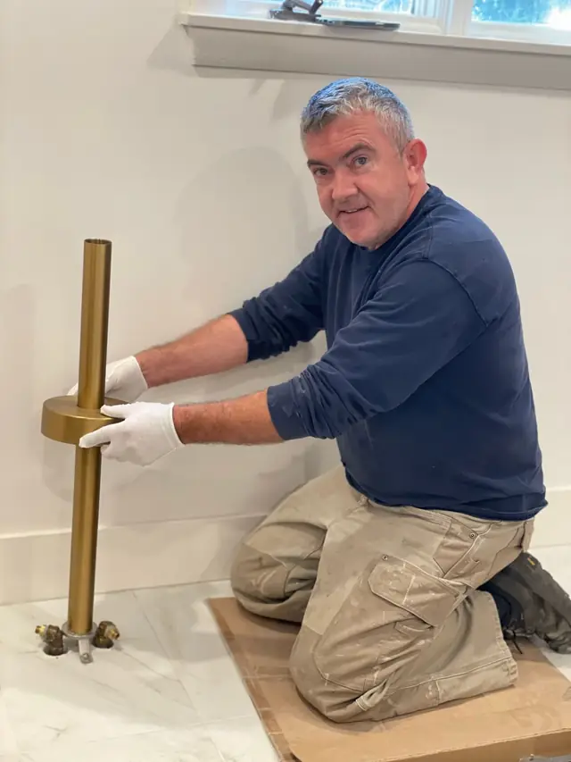 A brass floor-mount tub filler fixture being installed by hand