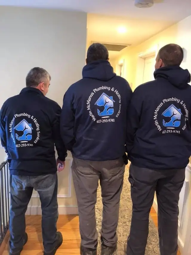 Three McManus crew members seen from behind in navy hoodies printed with the Martin McManus Plumbing & Heating logo and phone number